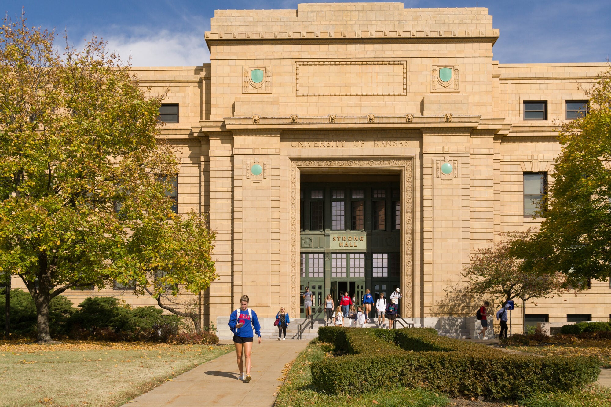 Students on the walk in front of a stone university hall.