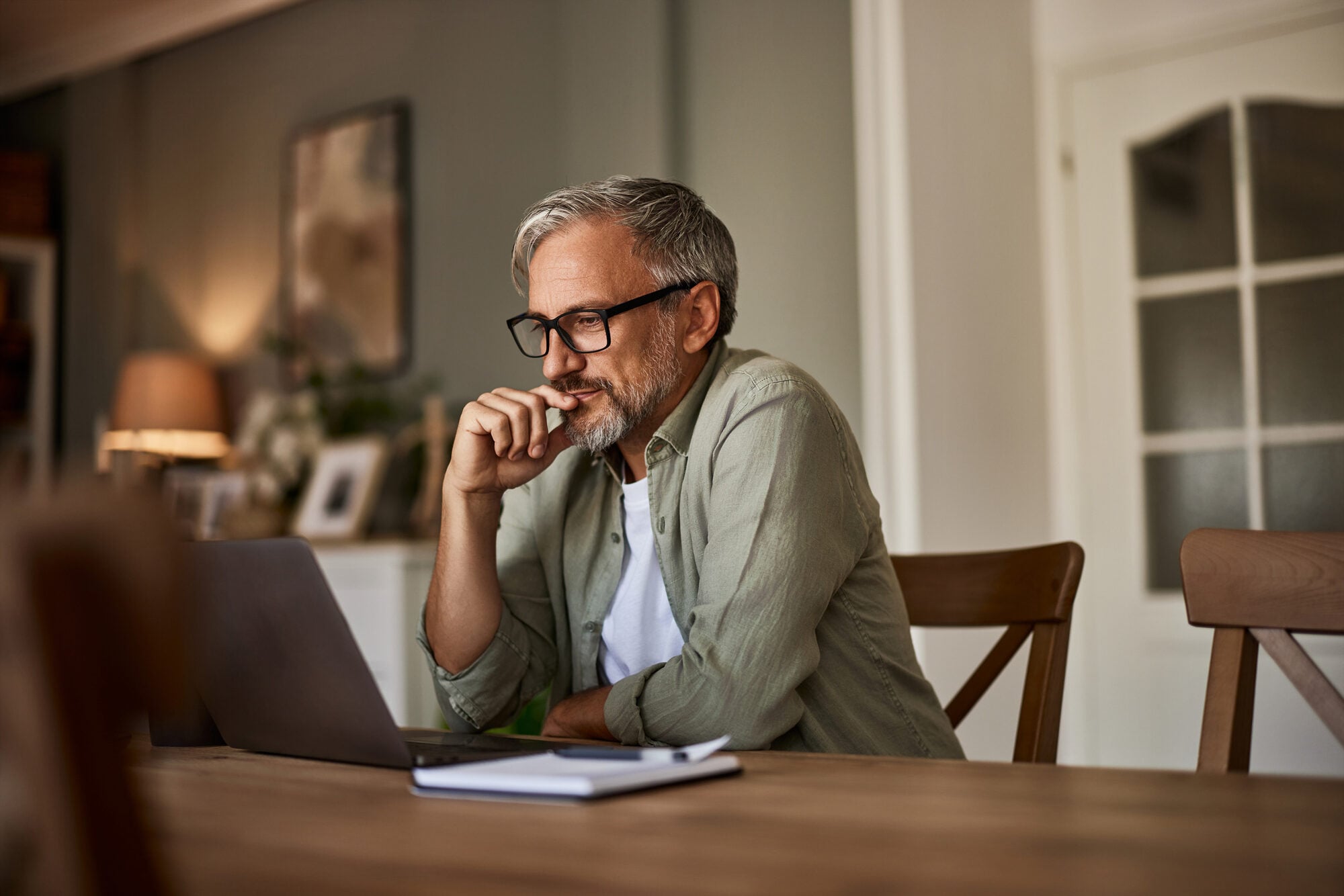 A man reading at a laptop at his dining table.